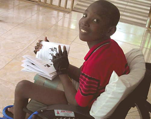 Photo of a Haitian boy in his wheelchair holding a book and looking over his shoulder at the photographer.