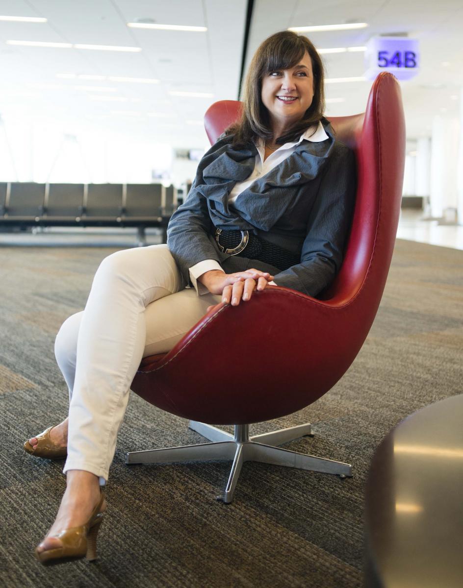 Photo of Virgin America’s Chief Marketing Officer Luanne Calvert sitting in a red chair in an airport waiting area near gate 54B. Photo by Toby Burditt
