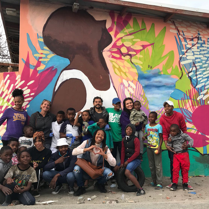 Libra Gutierraz stands in front of mural painting with kids