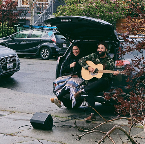 Two people sitting out of the back of a car, one with a guitar