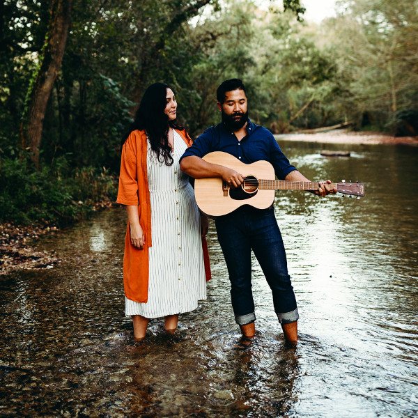 Two people standing in a shallow creek, one holding guitar