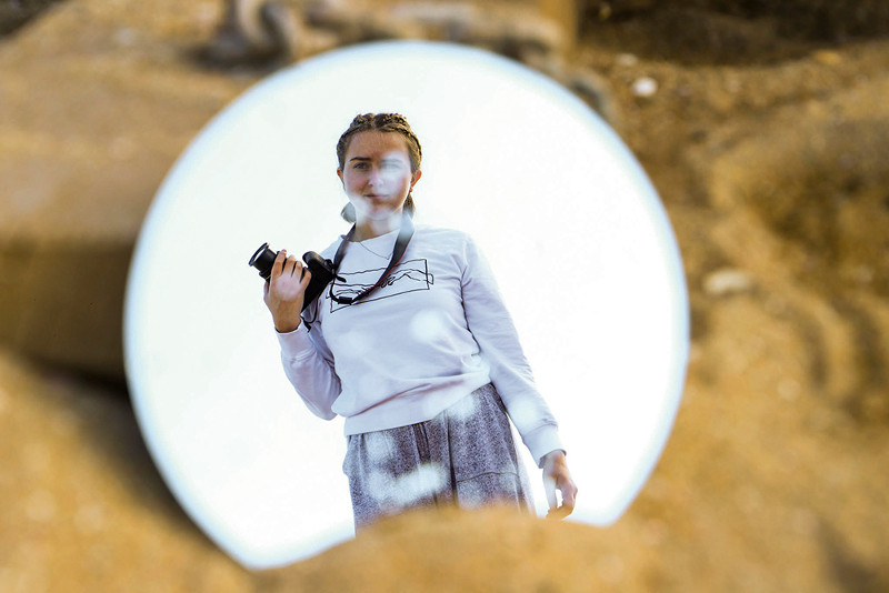Small circular mirror with reflection of a person holding a camera