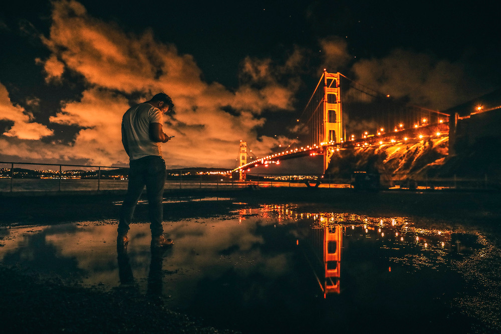 Person checking phone in front of the Golden Gate Bridge at night