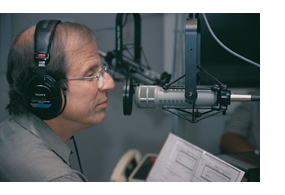 Michael Kransy waering headphones and speaking into the microphone at KQED.