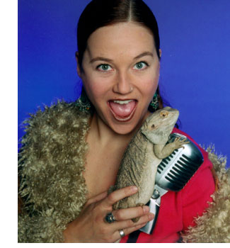 Alice Radio DJ Sterling James with a big smile holding an iguana and leaning against her microphone.