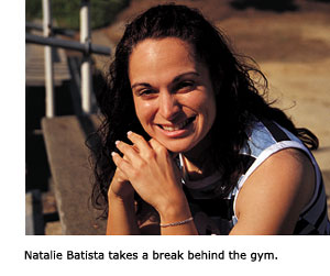 Natalia Batista, the new president of the Associated Students, sits on a set of bleachers behind the gym. She is smiling and resting her chin on her hands folded in front of her.