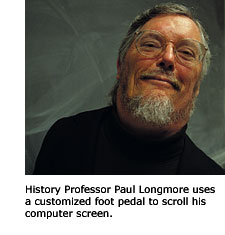 A head shot of History Professor Paul Longmore. He is smiling and seated in front of the blackboard in his classroom.