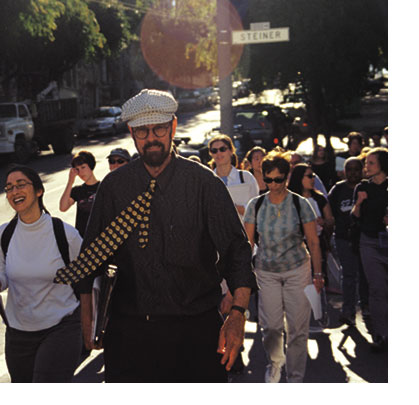 Geography Professor Max Kirkeberg walks at a brisk pace, his colorful tie with yellow circles swinging to the left with his students following behind. They are crossing Steiner Street during a tour of San Francisco’s Western Addition.