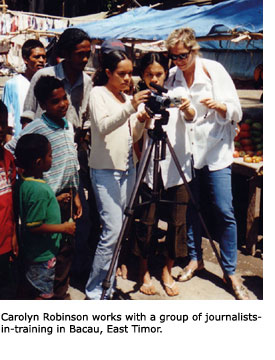 SFSU alumna Carolyn Robinson stands next to a group of boys and girls and shows them how to use a video camera in Bacau, East Timor.