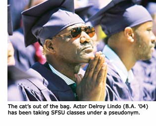 New grad Delroy Lindo in his cap and gown, arms folded as if in prayer, as he stands among a sea of fellow graduates.