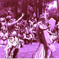 Students dressed in sixties garb, long-flowing shirts and skirts, dance and playfinger symbols as a crowd gathers on the quad to watch.