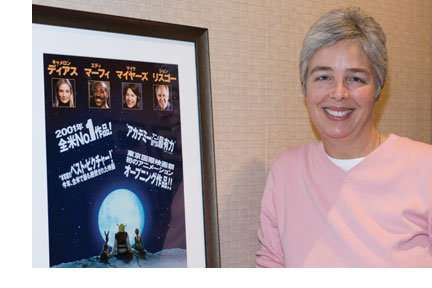 A smiling Gloria Borders stands beside a framed movie poster of Shrek at the Dreamworks studio.
