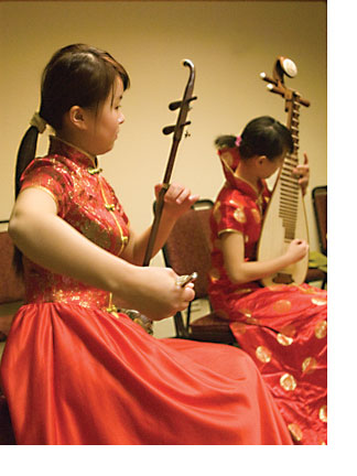 Two young women from China dressed in red and gold silk dresses play traditional Chinese instruments.