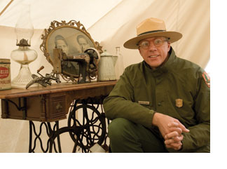Park ranger Bob Holloway sits inside one of his earthquake tents. The tent contains a period sewing machine, oil lamp, tea kettle and a family portrait in a gold antique frame.