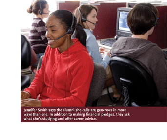 Student Jennifer Smith, wearing a red sweatshirt and telephone headset, smiles broadly as she talks with a potential donor by phone. Other students, wearing headsets, are in the background.