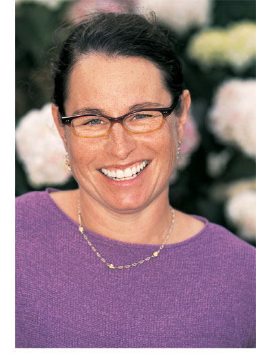 Professor Deborah Tolman smiles for the camera, a backdrop of pink flowers complements her lavender sweater.