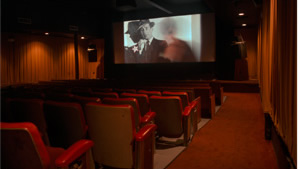 Photo of movie theater showing a Humphrey Bogart film, and a quote by Eddie Miller, "Till the day I die -- in a theatre, with any luck -- I'd rather wait on line for a movie, than download one online."