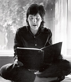 Rae Armantrout sitting down and reading a book.
