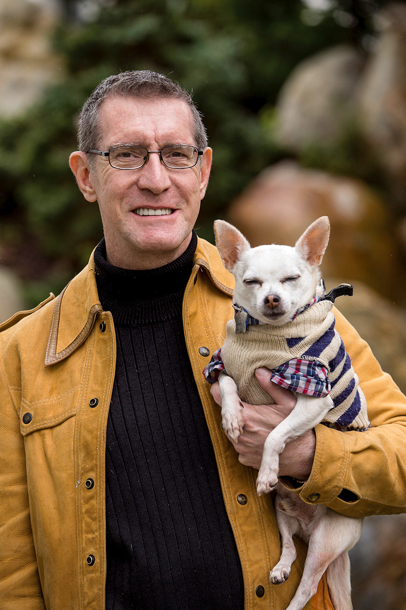 Garrick Wilhelm holding up his dog in a dog jacket