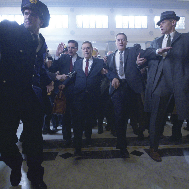 Men in suits and a policemen escorting a man