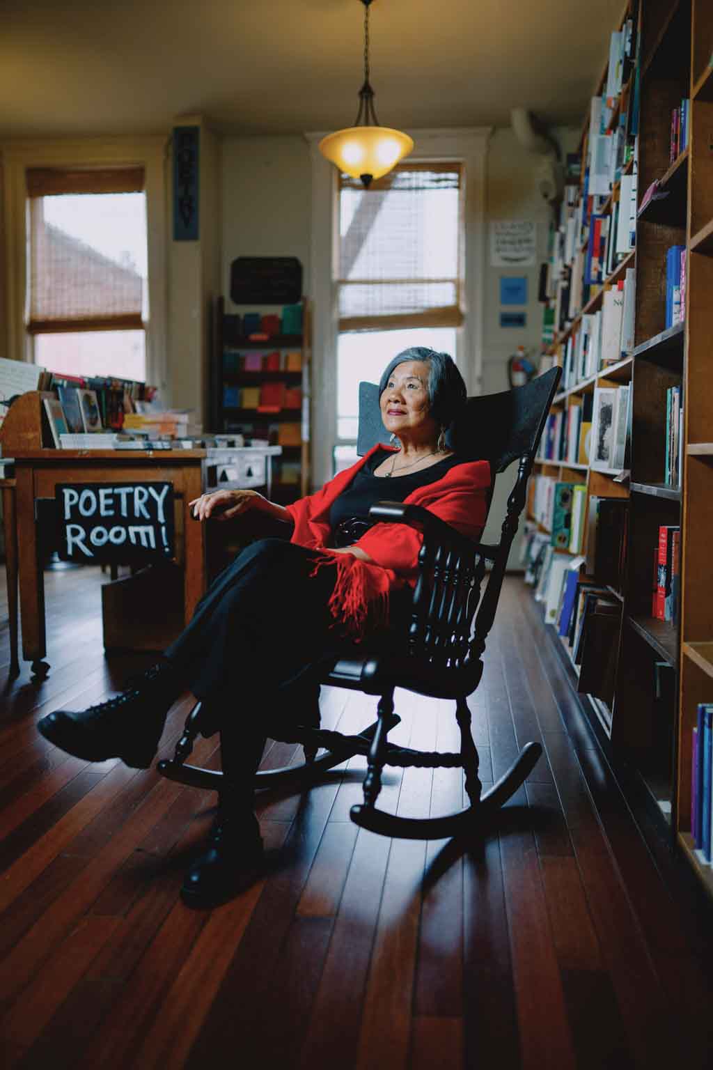 Genny Lim sitting on a rocking chair in the poetry section