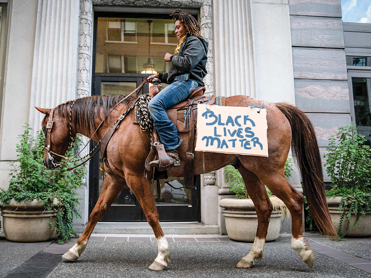 Woman riding a horse with a sign reading 'Black Lives Matter'