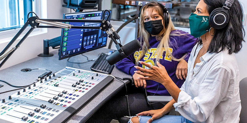 Two women wearing masks in an audio recording room