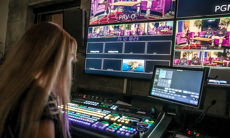 woman sitting in a live production studio in front of lit up buttons and multiple monitors