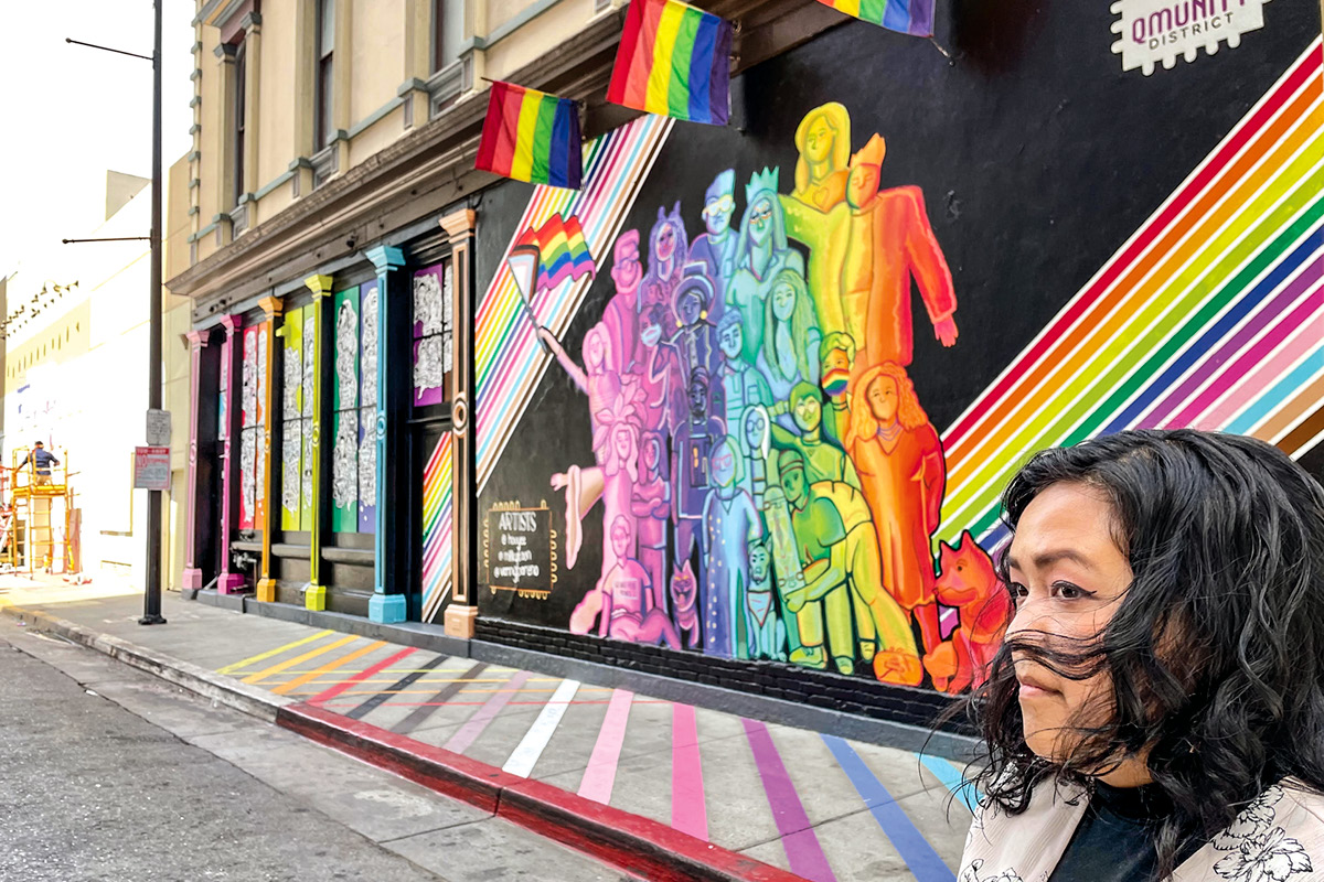 Houyee Chow standing in front of a LGBTQ mural