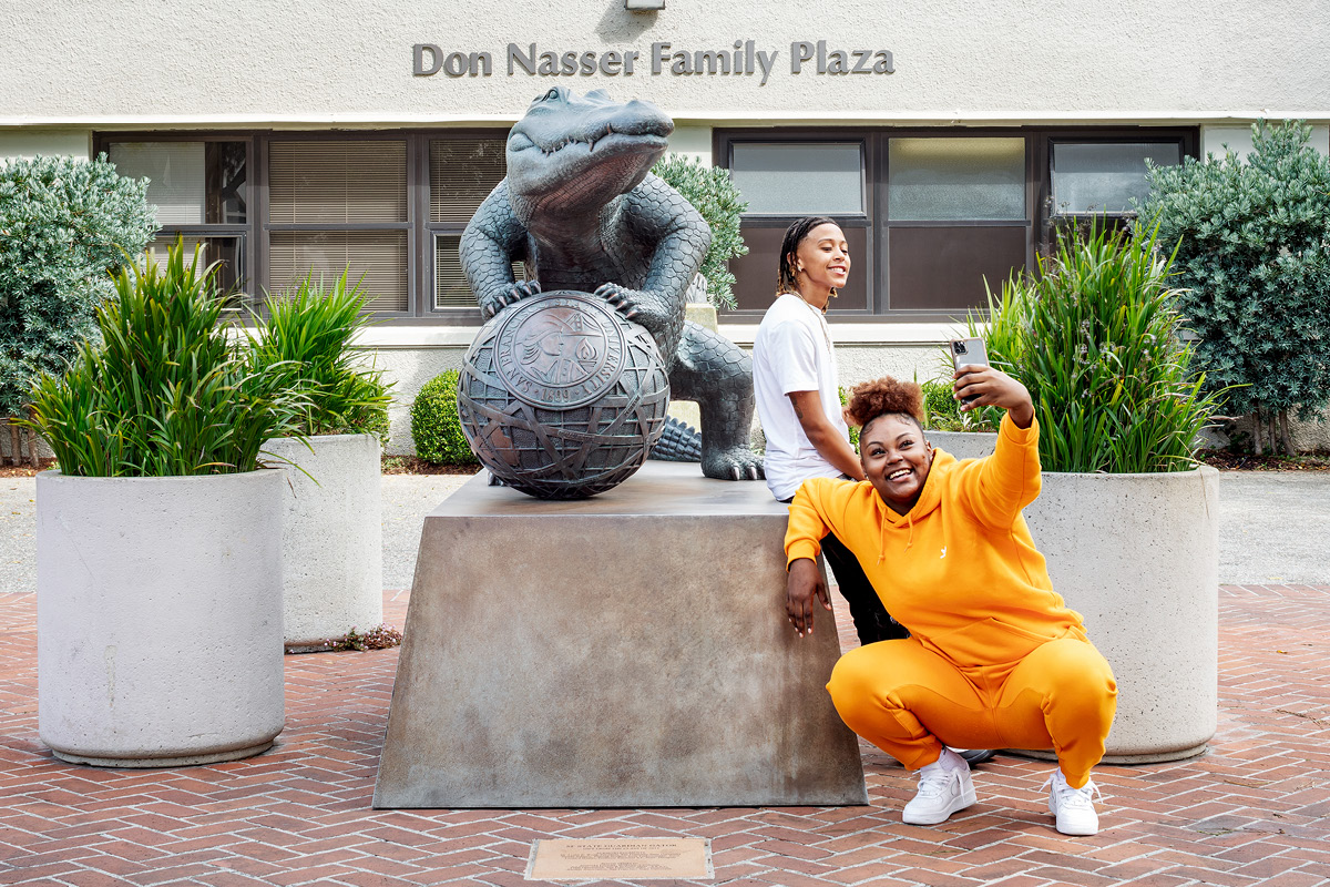 Two people taking a picture with a gator statue