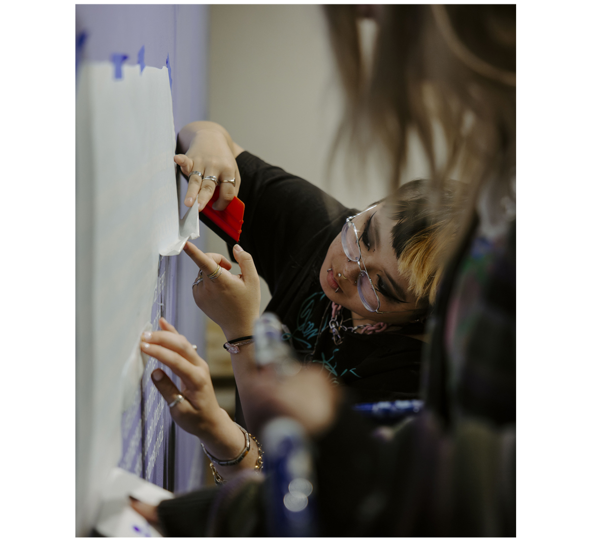 a student looking behind a sheet that contains text printed on a purple wall