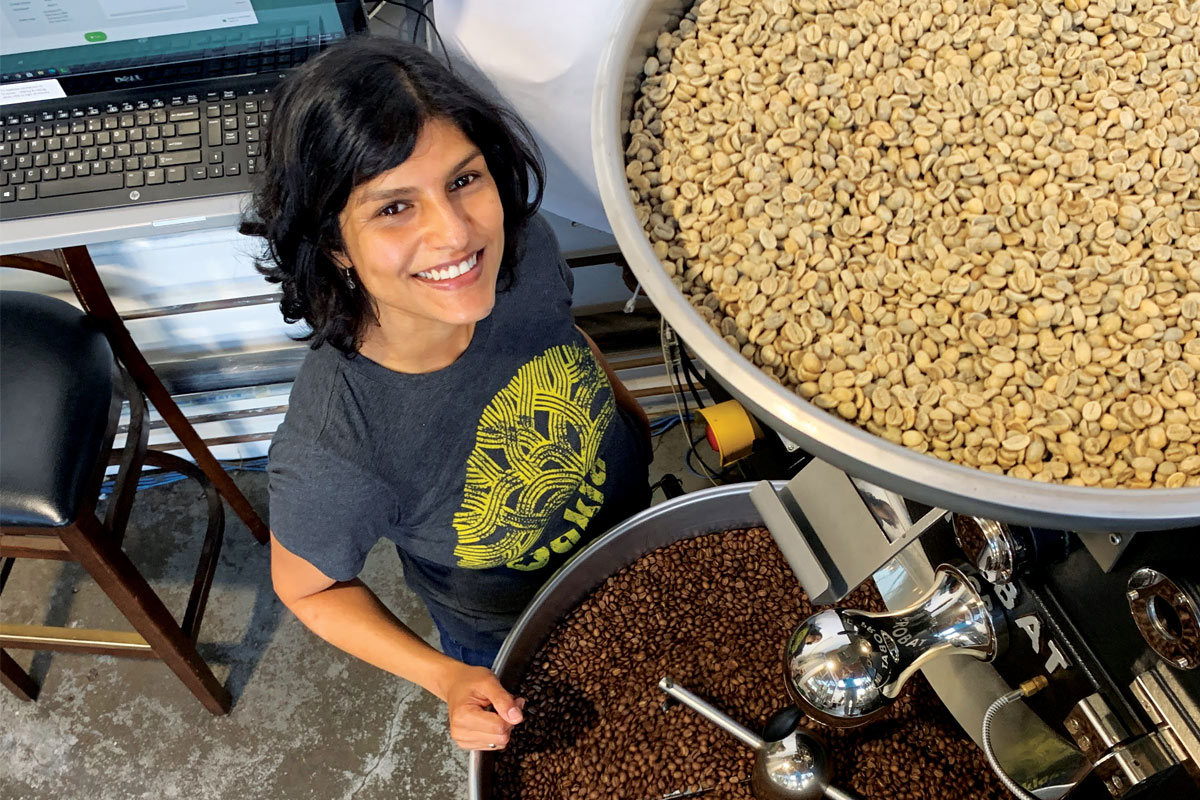 Tanya Rao smiling and standing next to coffee grinders filled with coffee beans