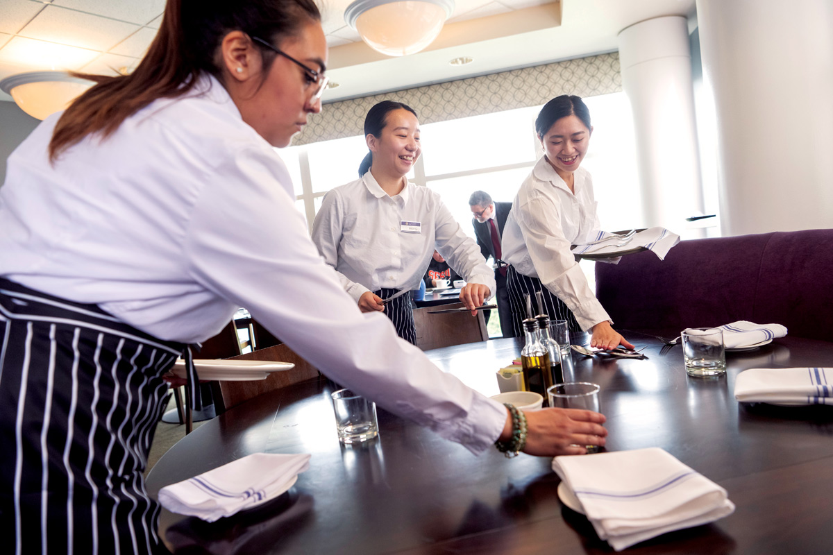 three student waiters cleaning and preparing a table for dining