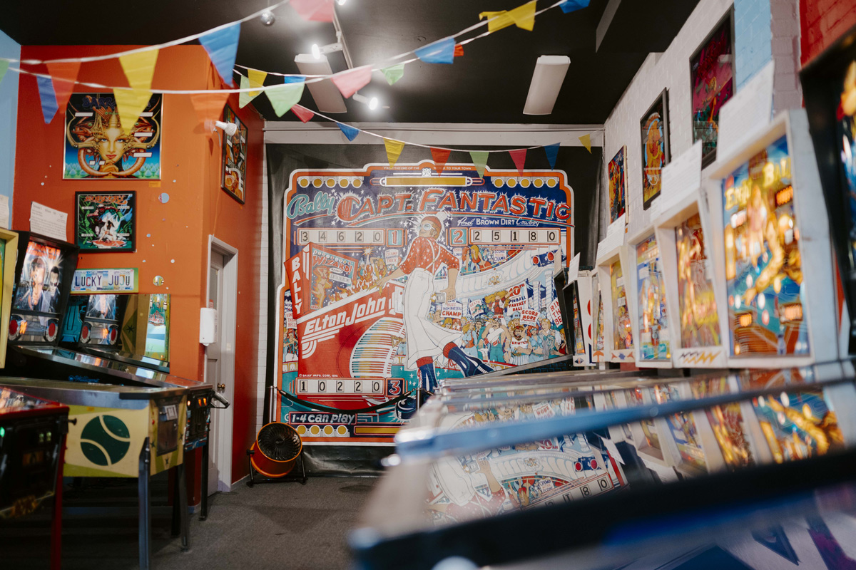 a decorative lobby with posters and lights, along the walls are 8 illuminated pinball machines