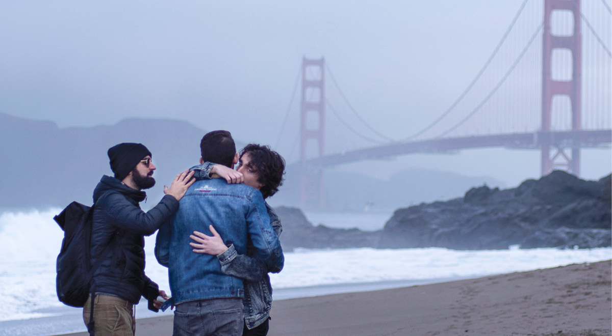 Couple hugging with another guy patting the man on the shoulder with the golden gate bridge in the background