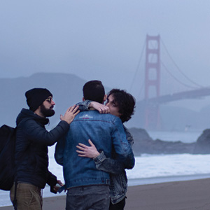 Couple hugging with another guy patting the man on the shoulder with the golden gate bridge in the background