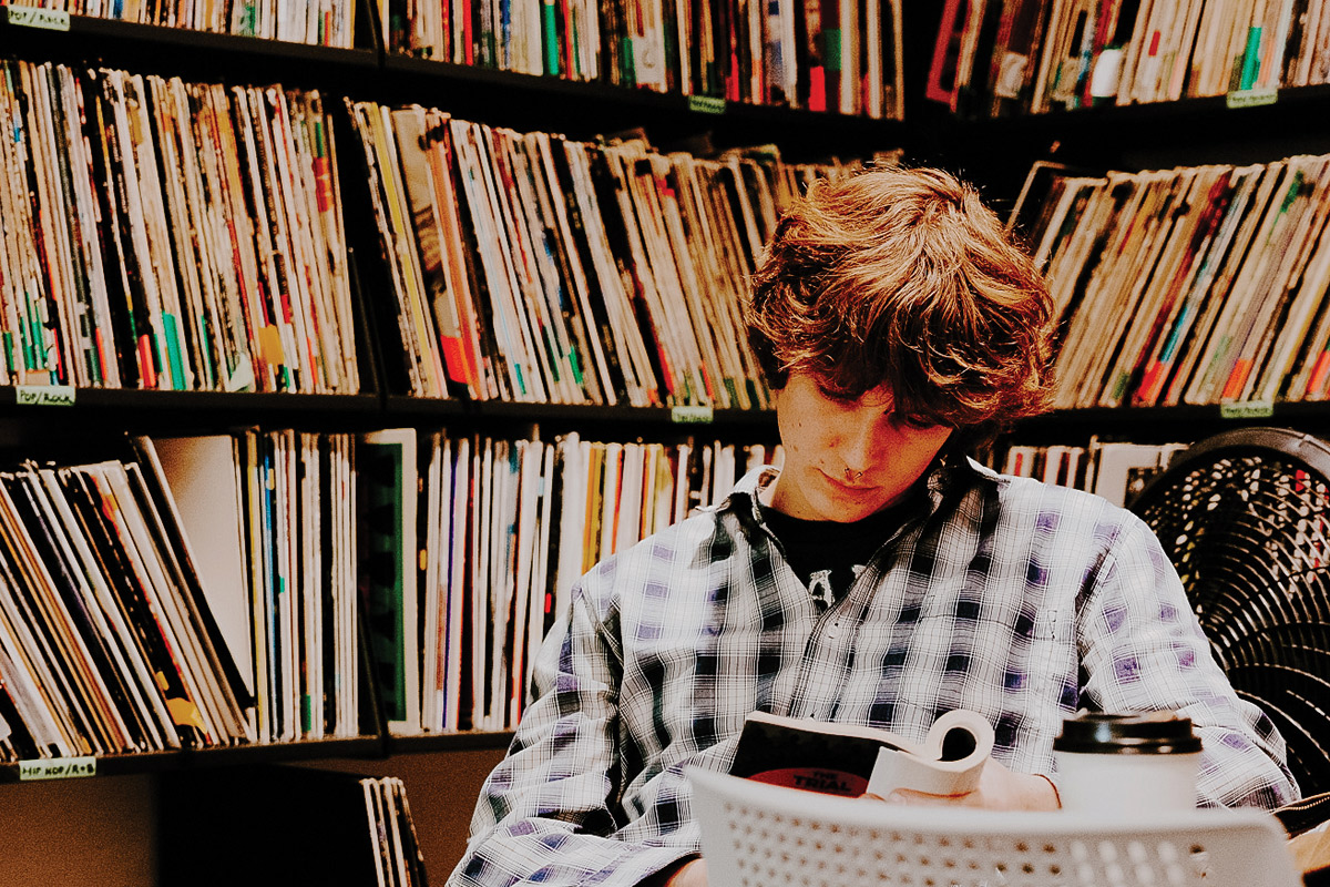 a student reading a book in a library with shelves full of vinyl records
