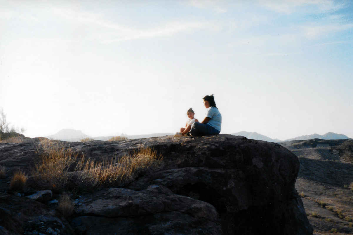 a woman and child sitting peacefully on a cliff